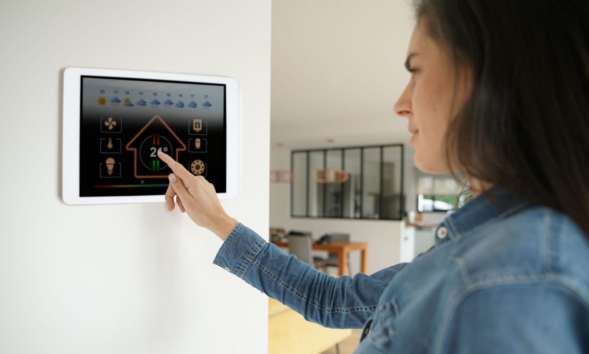 Woman in the home adjusting a device like a central heating thermostat, mounted on the wall