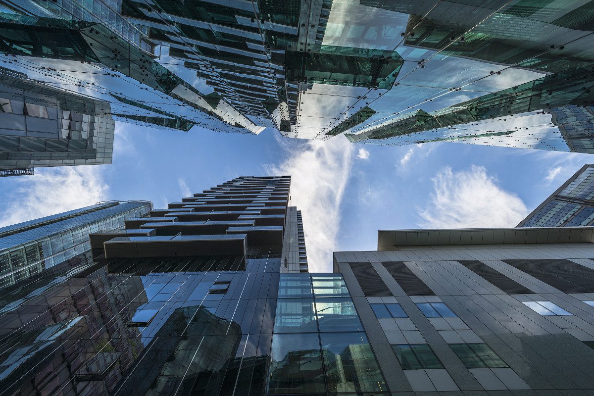 Skywards view from the bottom of two tall, modern buildings facing each other - blue sky and some cloud is visible in the distance, in the gap between the two structures