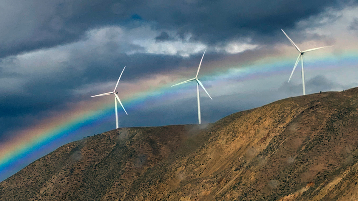 Wind turbines on a Scottish hillside with a rainbow cutting across the mid-level of the image