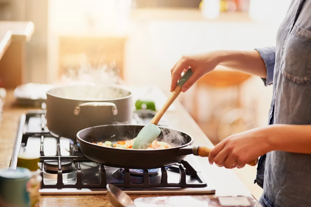 Cooking on a set of kitchen gas hobs, with steaming pots and the person's arms visible