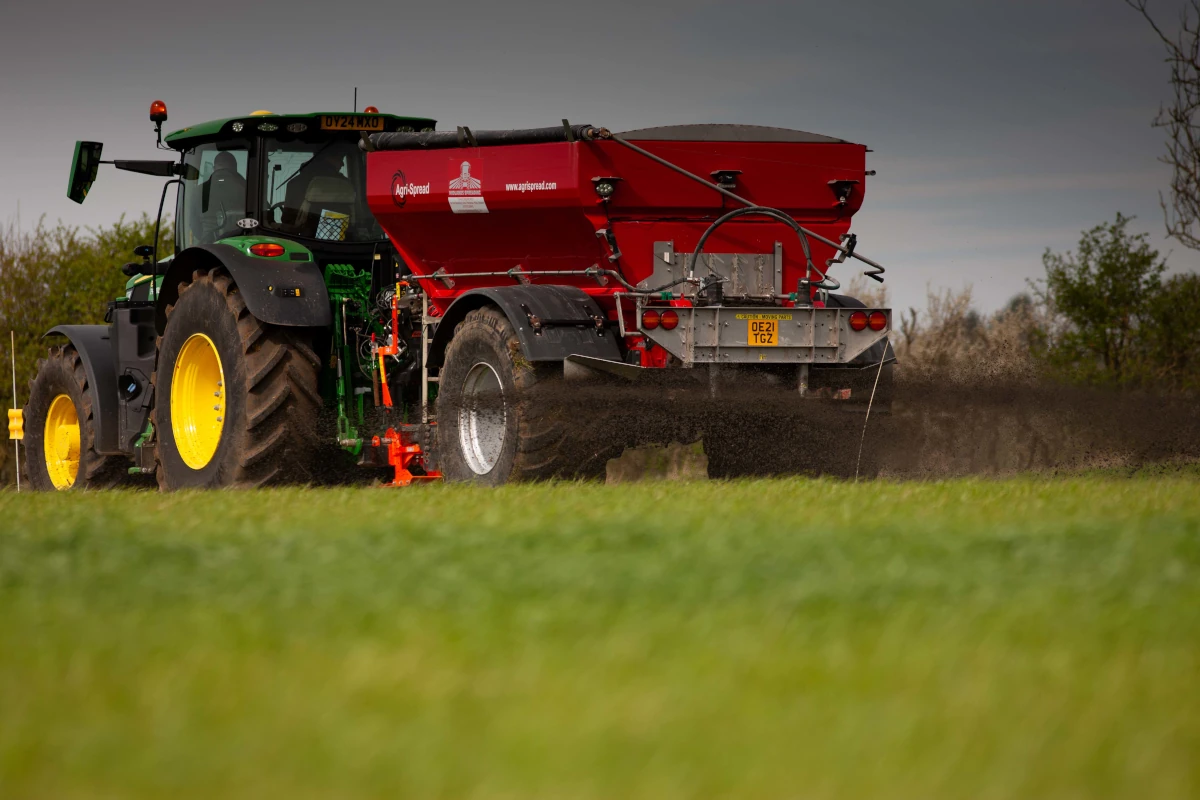 Tractor carrying a skip-like attachment on a trailer, seen in the distance, on a grassy surface